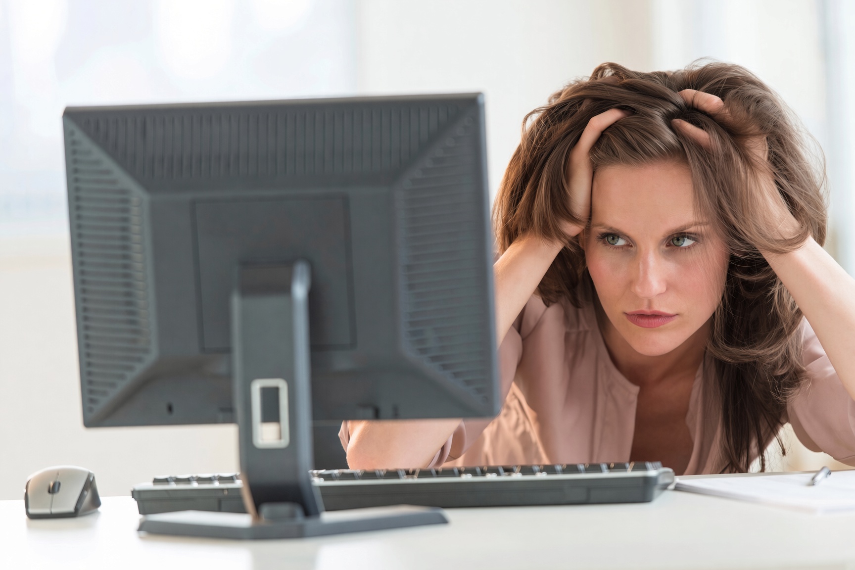 A frustrated woman gripping her hair while staring at a computer monitor