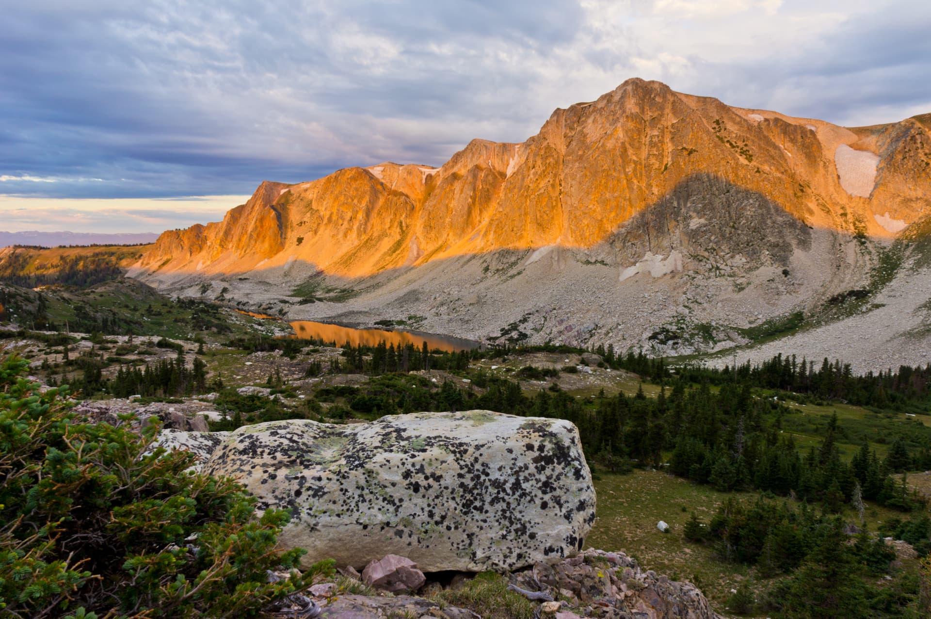 Alpenglow on a rugged mountain range above an alpine lake and pines at sunrise